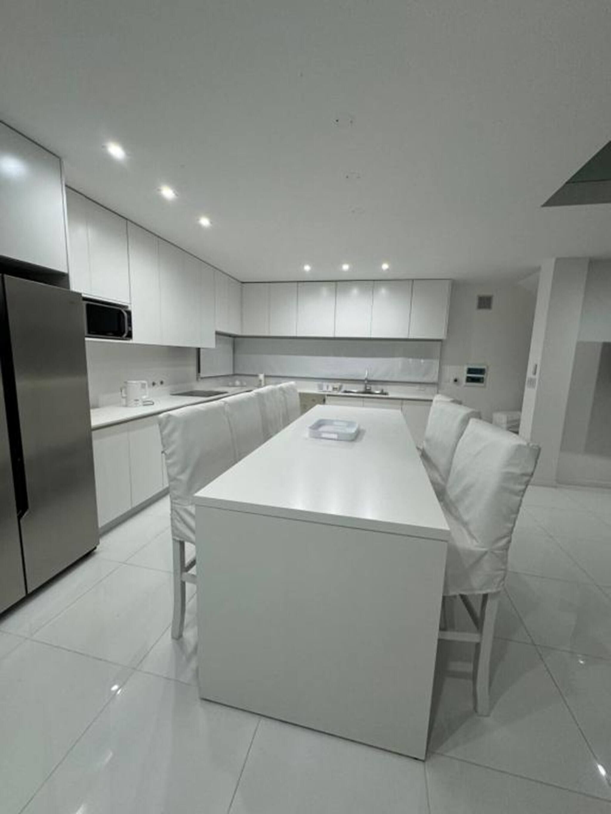 A modern kitchen with white cabinetry, a stainless steel refrigerator, and a central island with seating.