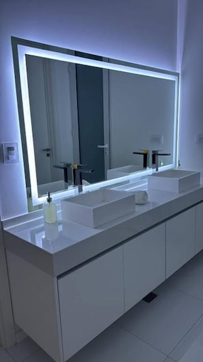 Un baño moderno con un espejo grande, dos lavamanos y un armario.