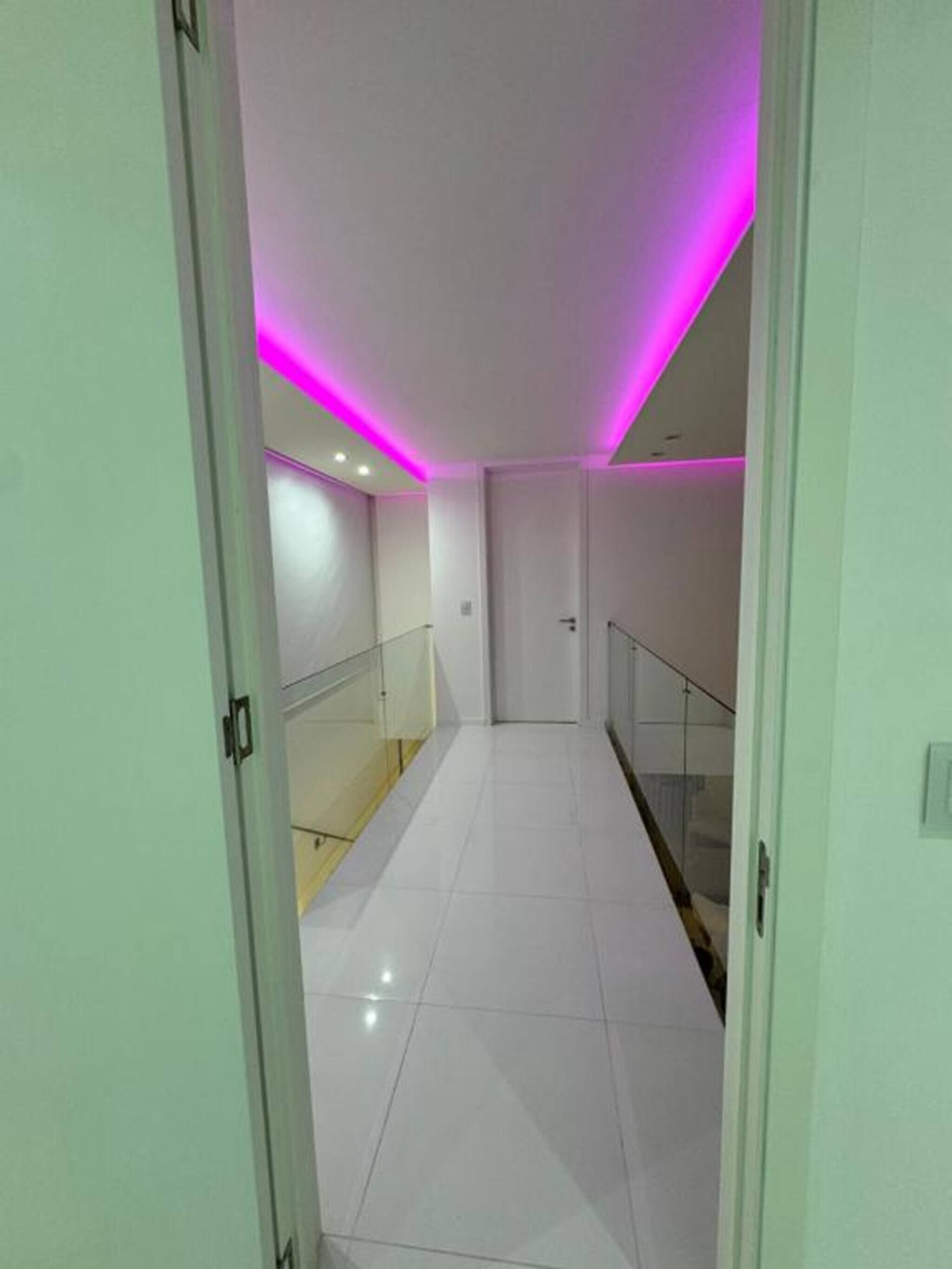 A hallway with white tiled floors and a glass railing on one side.