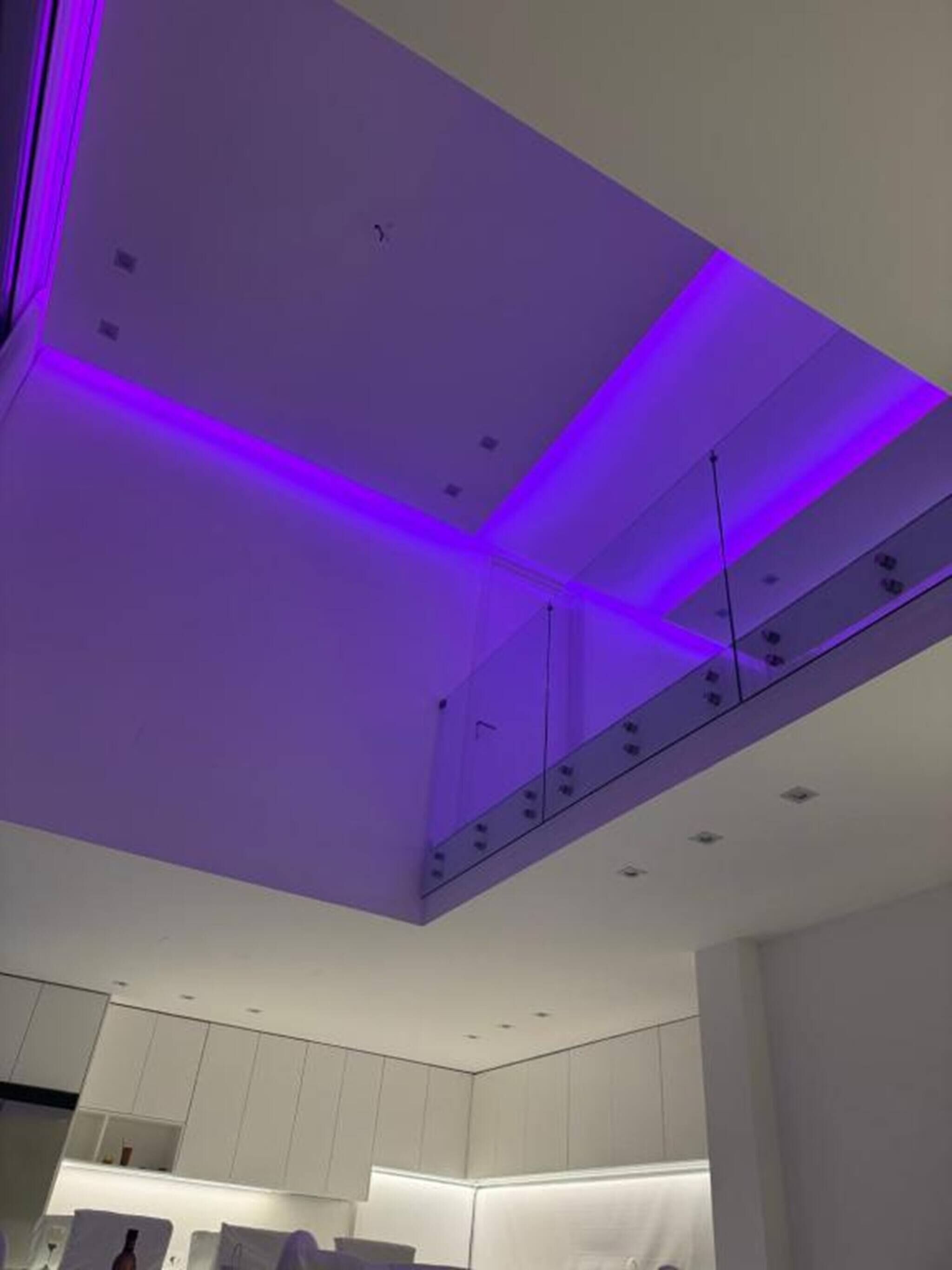 Een moderne keuken met witte kastjes en een paars plafondlamp.