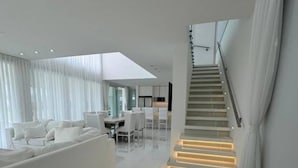 A modern living room with a white sofa, a dining area, and a staircase with illuminated steps. - Serena Boutique Potrero Garay (Alta Gracia)
