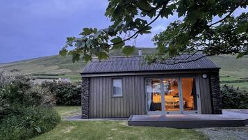 Una cabaña pequeña y rústica con cimientos de piedra, ventanas amplias y un porche.