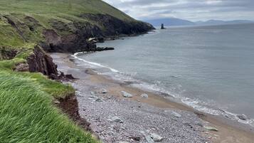 Un paisaje costero con una playa rocosa, zonas cubiertas de hierba y un faro a lo lejos.