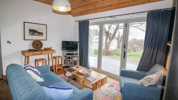 A modern living room with two blue sofas, a wooden coffee table, a TV on a stand, and a large window with curtains.