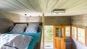 Ein Schlafzimmer einer Holzhütte mit einem Bett, Kissen und einem Fenster.