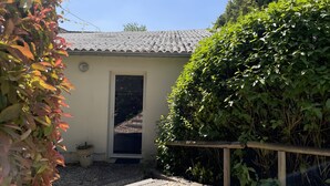 Un petit bâtiment avec un toit en tuiles, une porte et un chemin de gravier menant à l’entrée.