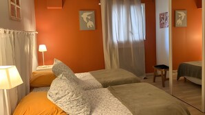 Une chambre avec deux lits, une fenêtre avec des rideaux, une lampe et des œuvres d’art accrochées aux murs.