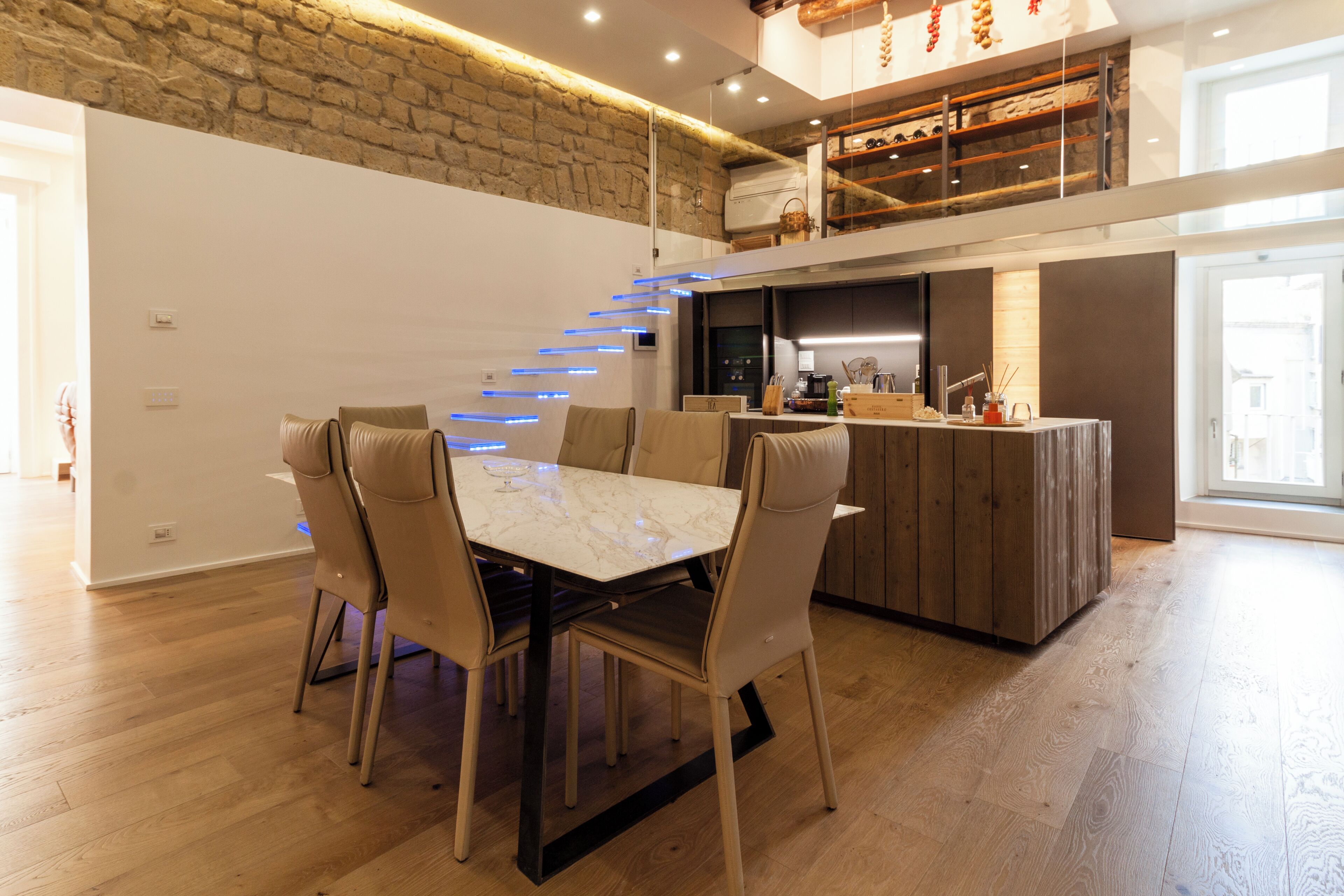 Une cuisine moderne dotée d’un îlot central, d’un coin repas avec une table en marbre et d’un escalier menant à un étage supérieur.