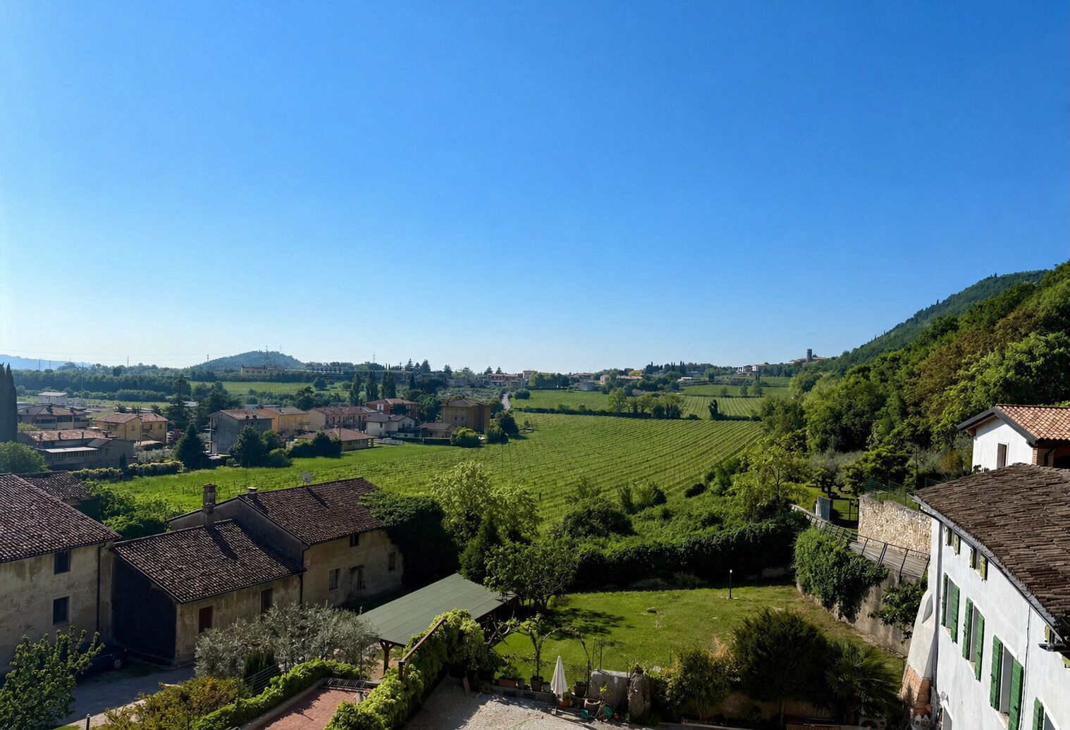 A rural landscape with terraced vineyards, traditional buildings, and a clear blue sky.
