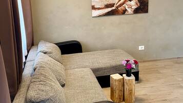 A living room with a sectional sofa, a painting on the wall, and a small wooden table with flowers.