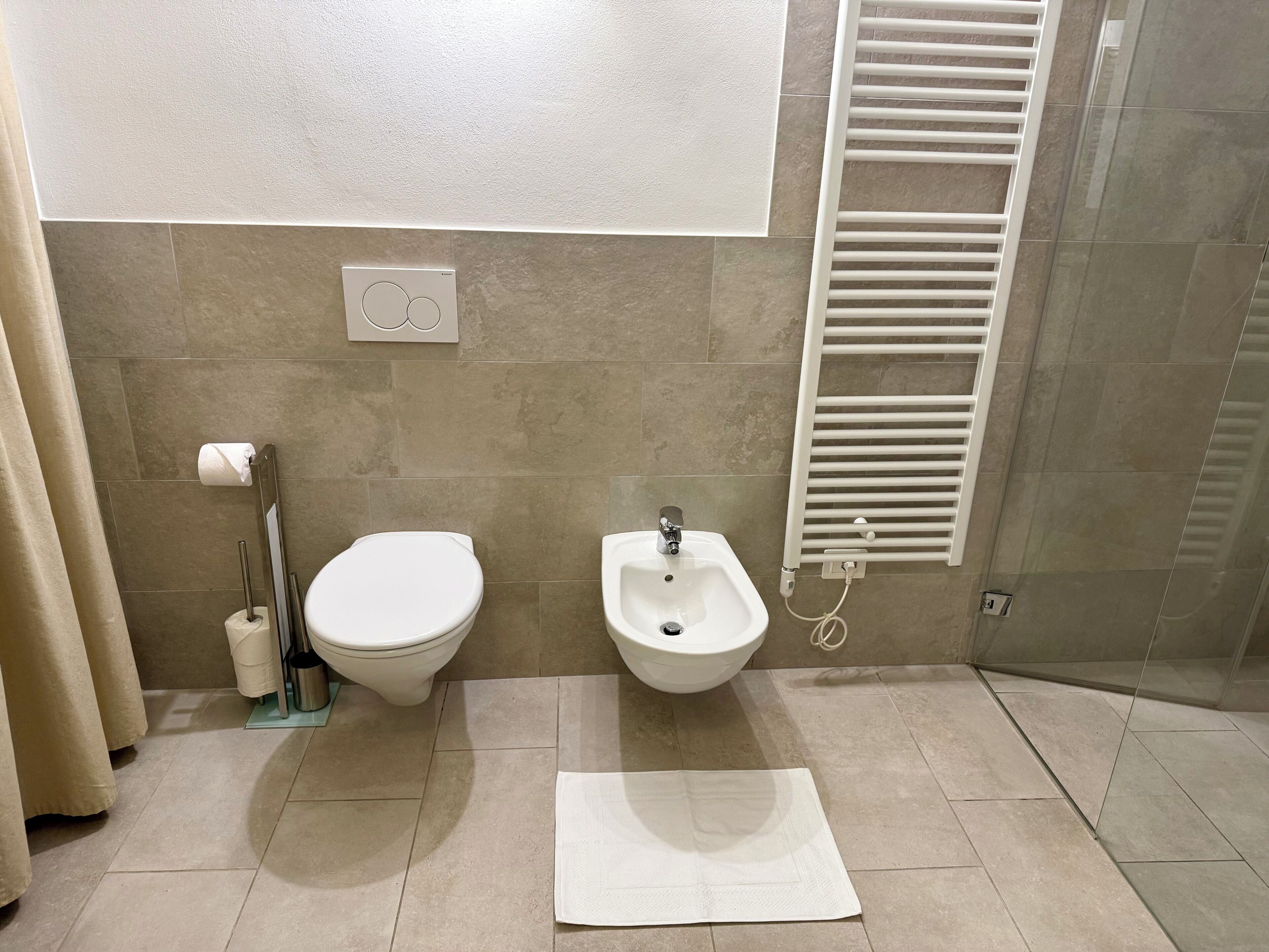 A bathroom with a toilet, bidet, towel, and a towel rack.