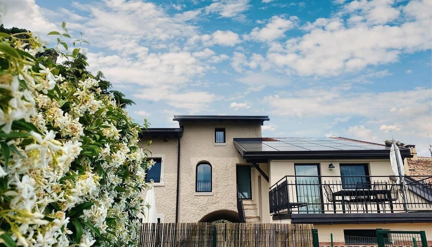Ein modernes, zweistöckiges Haus mit Balkon, Solaranlage und Garten mit weißen Blumen.