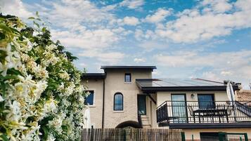 Ein modernes, zweistöckiges Haus mit Balkon, Solaranlage und Garten mit weißen Blumen.