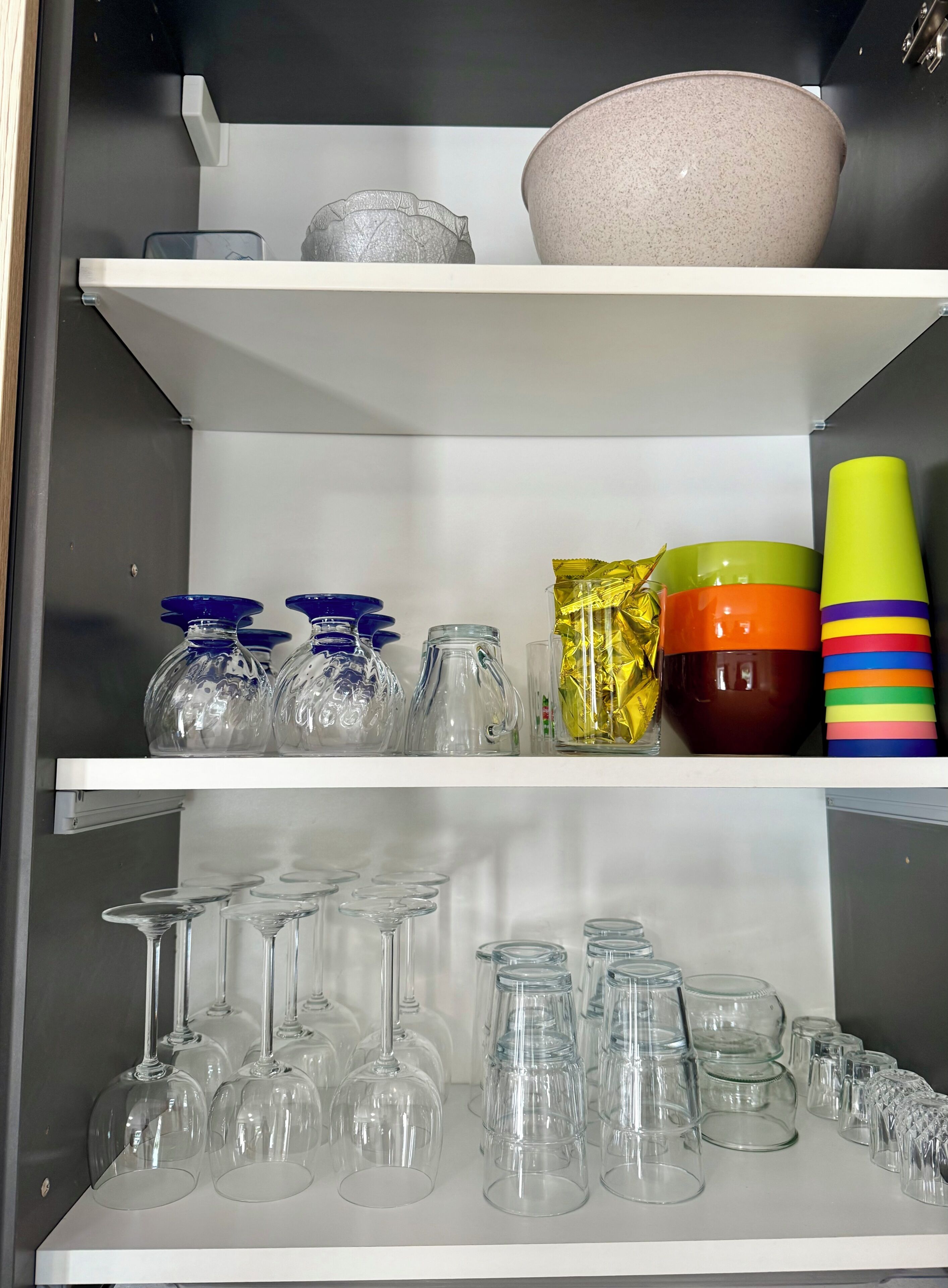 Uno scaffale con diversi bicchieri, tra cui calici da vino, bicchieri da cocktail e tazze decorative.
