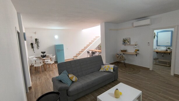 Una sala de estar moderna con un sofá gris, una mesita blanca y un comedor con sillas blancas.