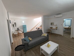 A modern living room with a grey sofa, a small white table, and a dining area with white chairs. - Abades South Beach Holiday Home with Private Terrace, Wi-Fi, and Air Conditioning (Abades)