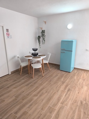Un coin repas avec une table ronde, quatre chaises, un réfrigérateur bleu et une plante suspendue.