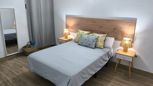 Un dormitorio ordenado con una cama, dos mesitas de noche, un tocador, un espejo y un cabecero de madera.