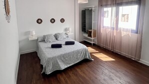 Une chambre à coucher comprenant un lit, des lampes de chevet, un luminaire suspendu, une armoire et une fenêtre avec des rideaux.