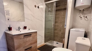 Une salle de bain moderne avec un meuble-lavabo en bois, une cabine de douche en verre et des toilettes blanches.