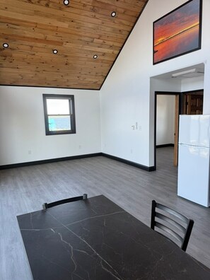 A room with a dark marble table, a wooden ceiling, a window, and a white refrigerator.