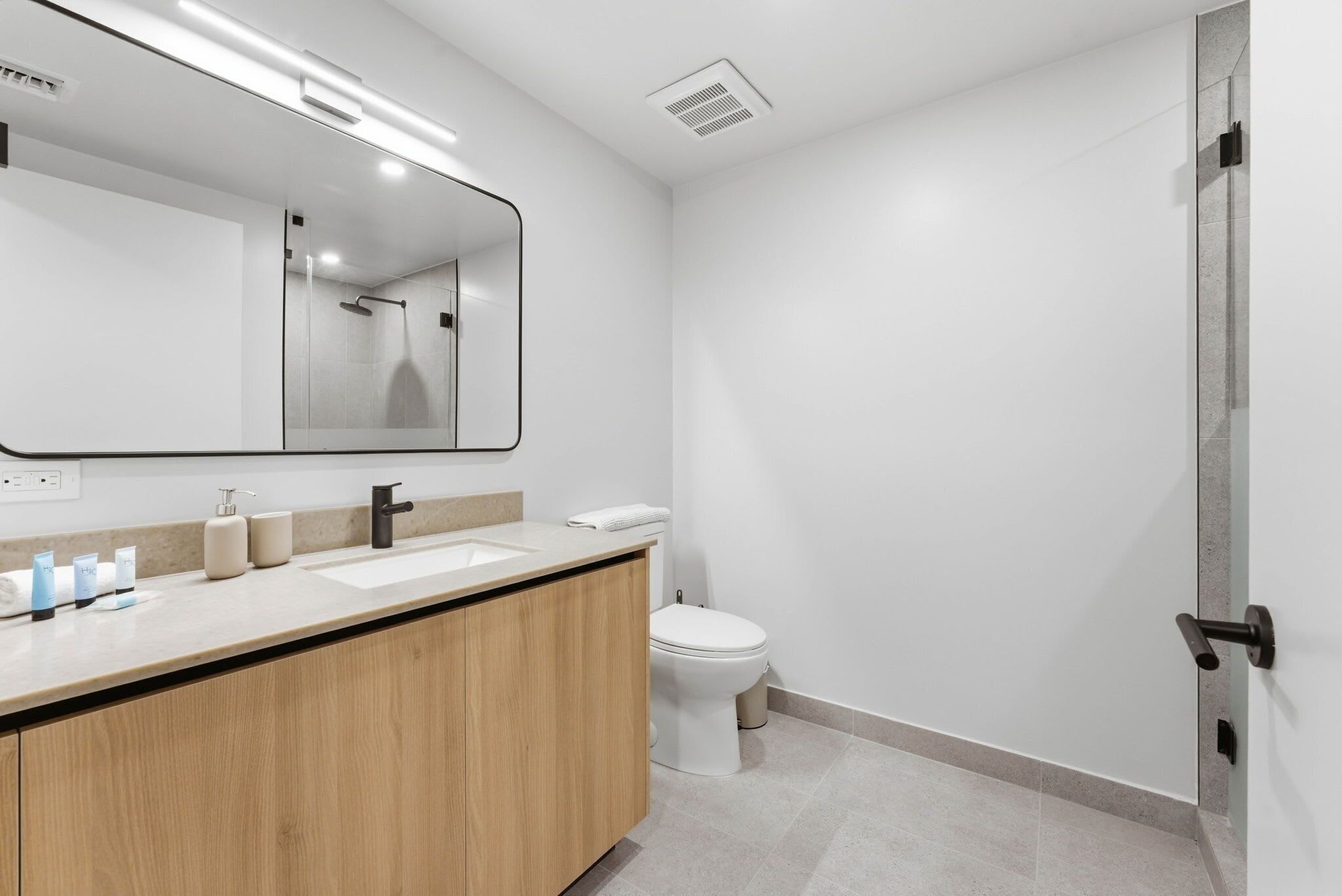 A modern bathroom with a wooden vanity, a large mirror, a toilet, and a shower area.