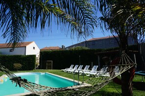 Ein Swimmingpool mit Hängematte, weißen Liegestühlen und einer Hecke.