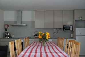 A modern kitchen with white cabinets, a microwave, and a refrigerator. There is a table with a red and white checkered tablecloth and a vase with sunflowers.