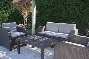 An outdoor patio with wicker furniture, including a sofa and two chairs, and a small table.
