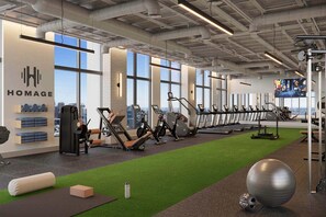 Ein modernes Fitnessstudio mit Trainingsgeräten, einer Grünflächen-Trainingsfläche und großen Fenstern mit Blick auf die Stadt.