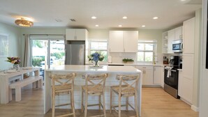 A modern kitchen with white cabinetry, a central island with bar stools, a built-in oven, and a refrigerator. - Turfside Terrace, Heated Pool and Putt Putt (Jupiter)