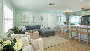 A modern living room with a grey sectional sofa, a small coffee table, and a dining area with wooden chairs and a white table. - Turfside Terrace, Heated Pool and Putt Putt (Jupiter)