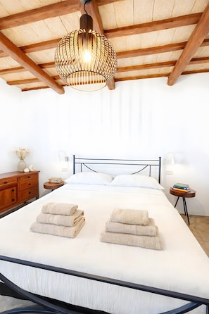Ein Schlafzimmer mit einem Bett, Nachttischen, einer hölzernen Kommode, einer Pendelleuchte und einer weißen Decke.