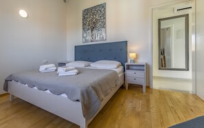 A neatly made bed with white linens and a grey blanket, a bedside table with a lamp, and a large mirror on the wall. - Lotus Elite Villa with Pool & Jacuzzi 7 (Pula)