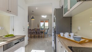 Eine moderne Küche mit Essbereich, inklusive Geschirrspüler, Kühlschrank und einer Holzausziehtheke mit Tassen und einer Schüssel.