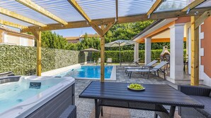 Zona de piscina exterior techada con un jacuzzi, sillas de descanso y una mesa con un cuenco de fruta.