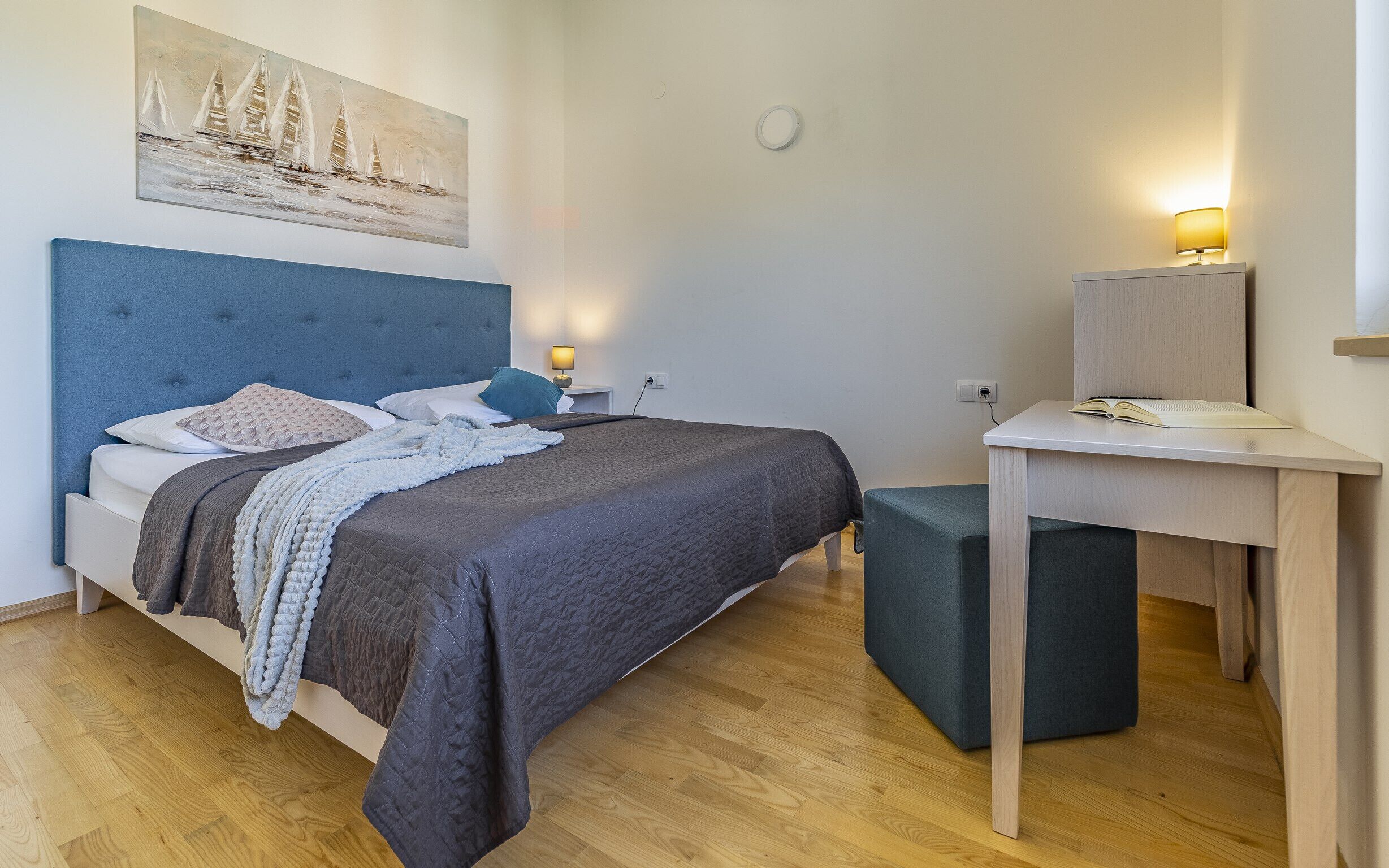 A neatly arranged bedroom with a bed, bedside table, lamp, and a desk with a chair.