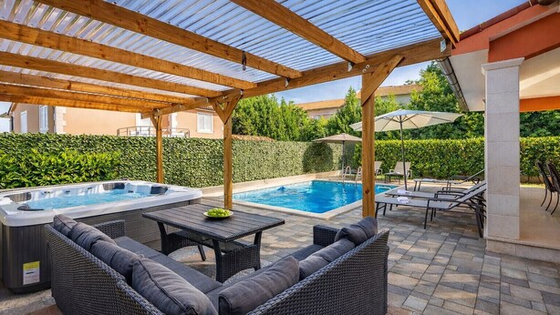 Uma área externa coberta com hidromassagem, espreguiçadeiras e piscina.