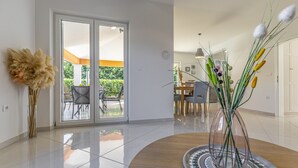 Una sala de estar moderna con un ventanal que da a un espacio exterior, una mesa de comedor y un jarrón decorativo con plantas.