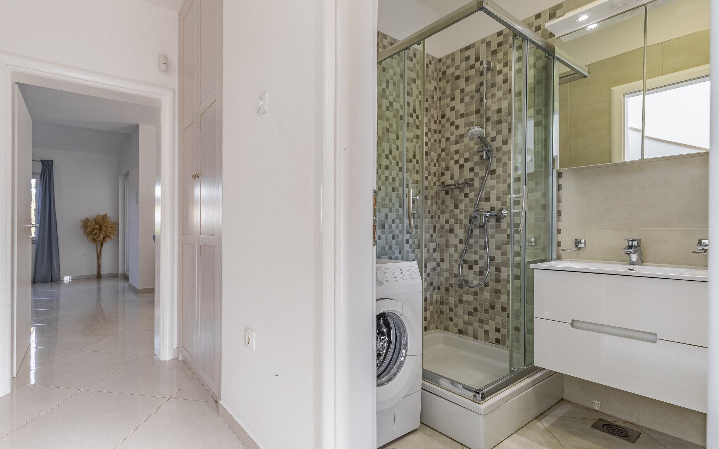 Une salle de bain moderne avec une douche à parois de verre, un lave-linge et un lavabo avec un miroir.