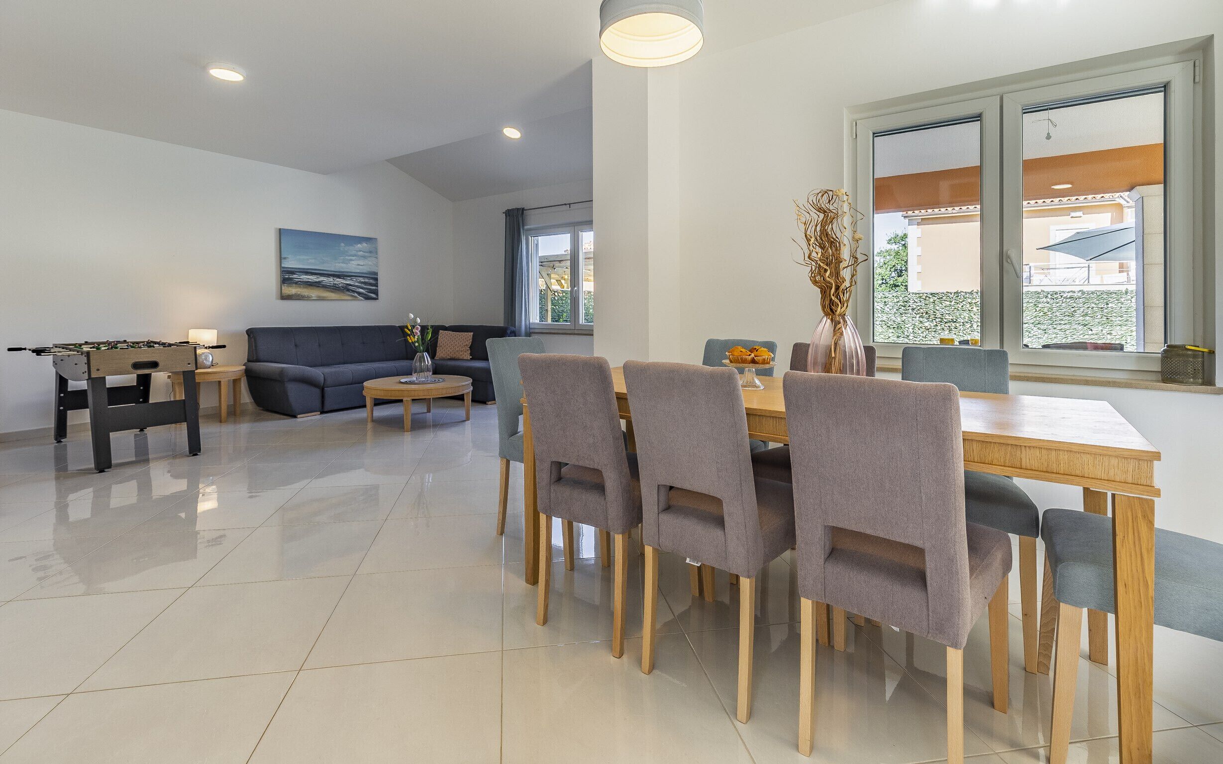 Una sala moderna con un sofá, una mesa de comedor con sillas y una mesa de futbolín.