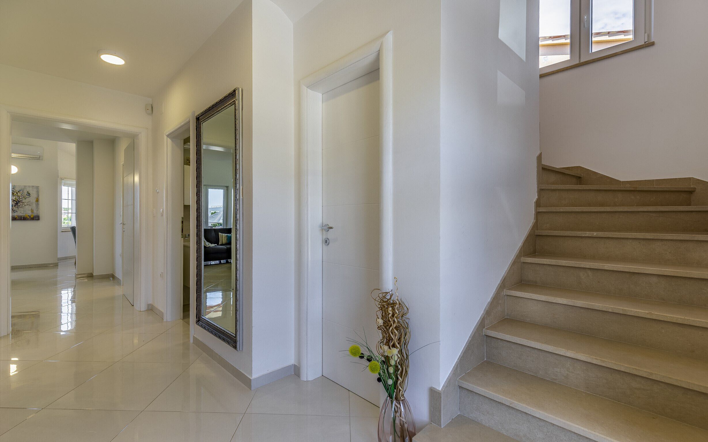 Un hall d’entrée spacieux, agrémenté d’un grand miroir, d’un escalier et d’un vase rempli de fleurs.