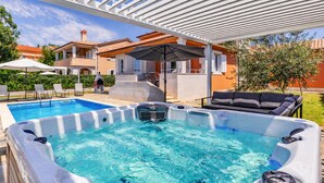 Ett bubbelbad med en pergola ovanför, en pool och utomhusmöbler.