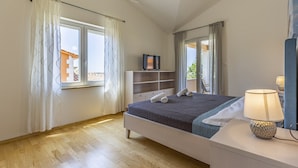 A bedroom with a bed, a bedside table with a lamp, a TV on a stand, and a wardrobe. - Lotus Elite Villa with Pool & Jacuzzi 1 (Pula)