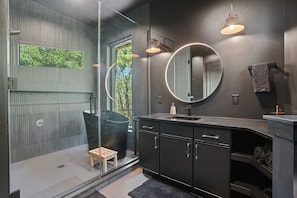 A modern bathroom with a glass shower enclosure, a round mirror, and a dark-toned vanity.