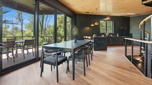 A modern kitchen with a large island, a dining area with a table and chairs, and a view through large windows. - The Outlook Treehouse & Lavender Farm (Oxford)