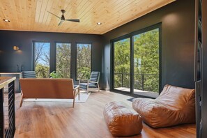 A modern interior with a wooden ceiling, large windows, a sofa, a chair, and a dining area.