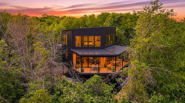 A modern house with a glass facade, surrounded by dense greenery.