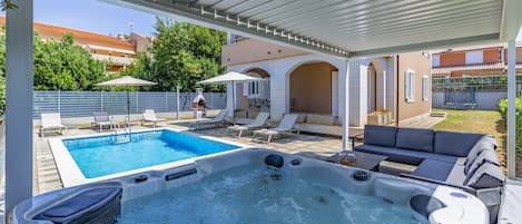A swimming pool with a hot tub, lounge chairs, and umbrellas.