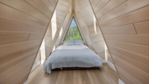 Une pièce triangulaire en bois, avec un lit et une fenêtre.